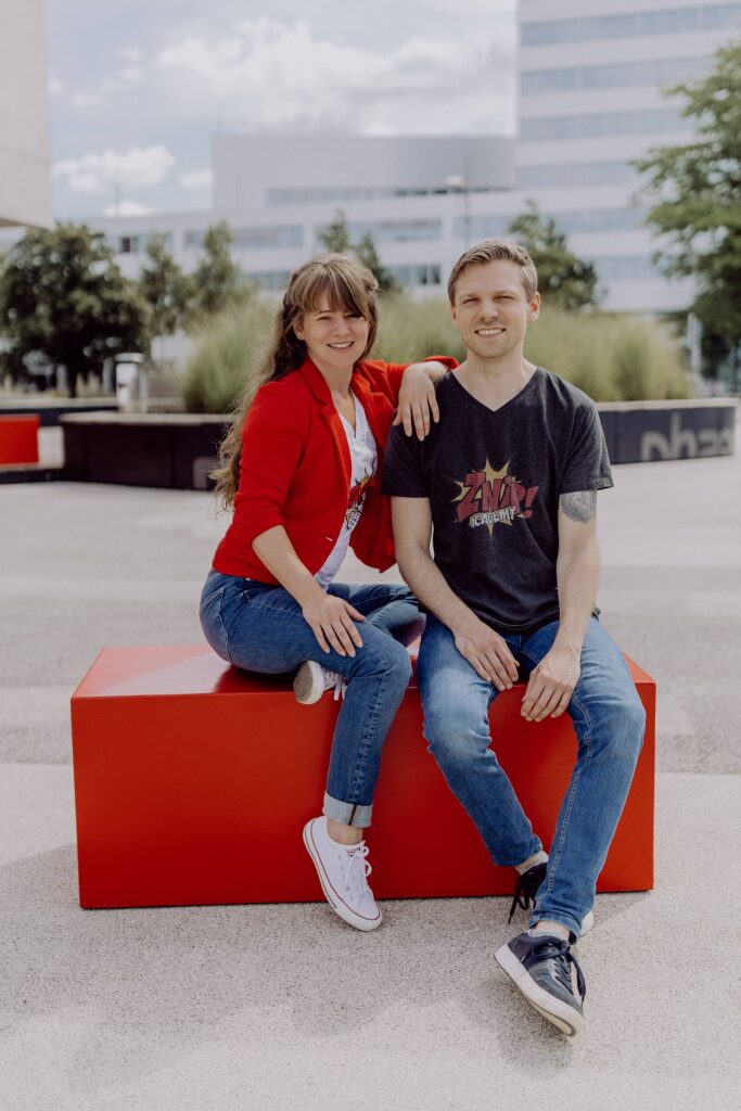 Janina Kappelhoff & Henry Schneider sitzen vor dem Phäno auf einem roten Block
