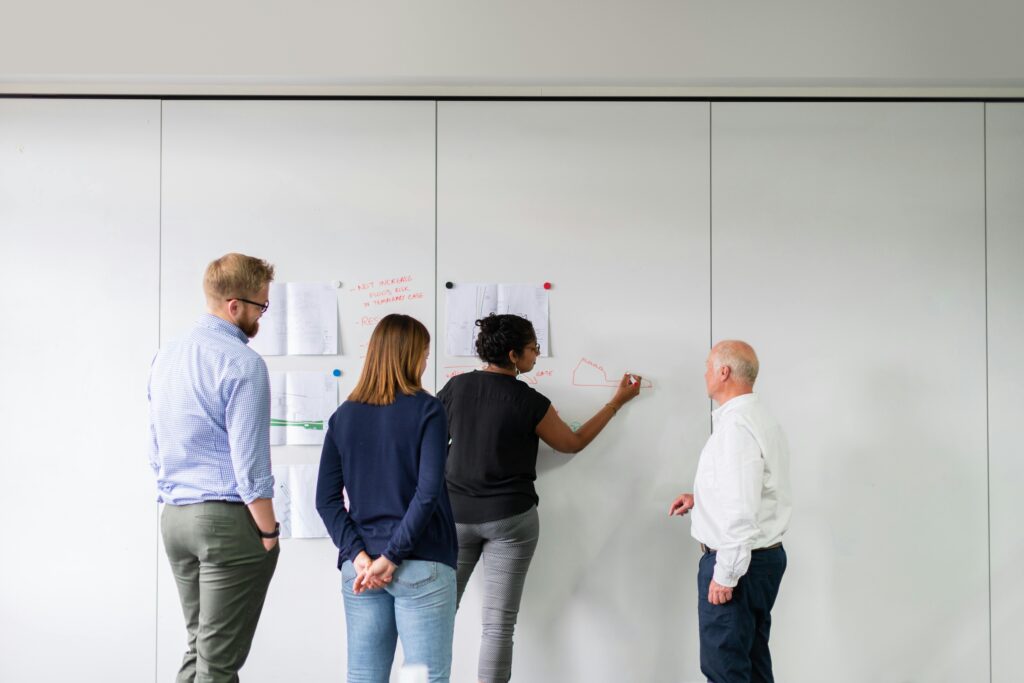 4 Menschen arbeiten gemeinsam auf Zetteln an einer Wand
